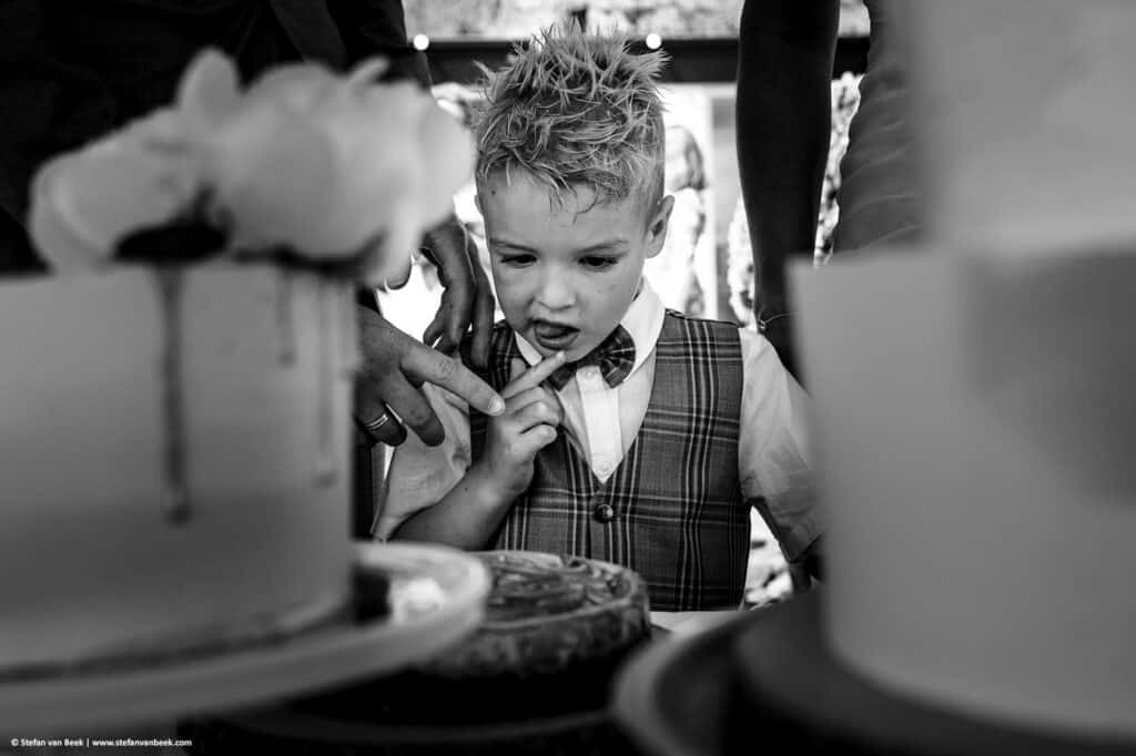 Bruidsjongen likt zijn vingers af bij zien van de taart maar krijgt een vinger van bruidegom als waarschuwing dat hij nog niet mag pakken © Stefan van Beek Fotografie