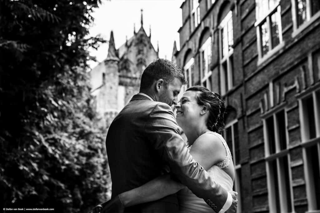 Bruidspaar heeft elkaar vast tegenover elkaar met glimlach op gezicht in historische centrum van Leiden en Hooglandse kerk op achtergrond © Stefan van Beek Fotografie
