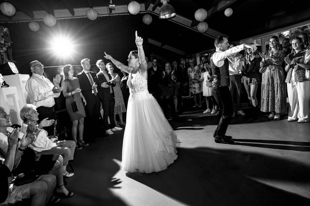 Bruid en bruidegom zijn omringd door hun gasten en hebben net na hun openingsdans hun handen in de lucht om het bruidsfeest te starten © Stefan van Beek Fotografie
