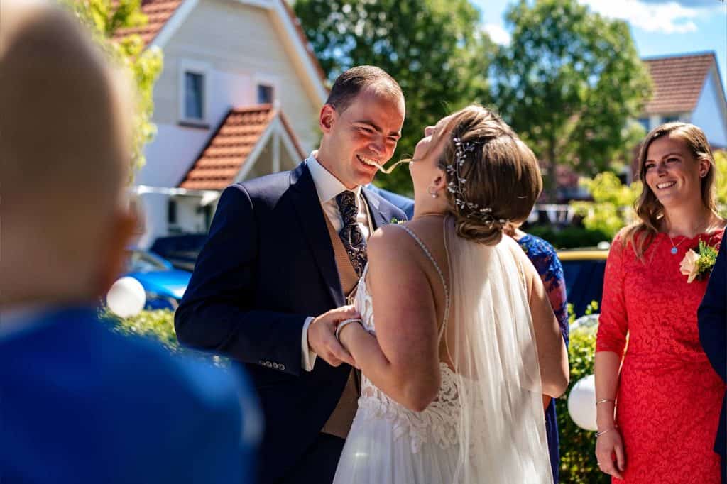 Bruid staat tegenover bruidegom bij first look en lacht met gezicht omhoog omringd door familie © Stefan van Beek Fotografie