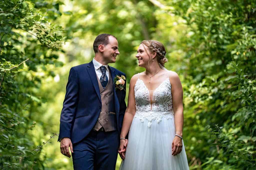 Bruidspaar loopt hand in hand en kijkend naar elkaar tussen de groene struiken en bladeren door bij bruiloft in Westland © Stefan van Beek Fotografie