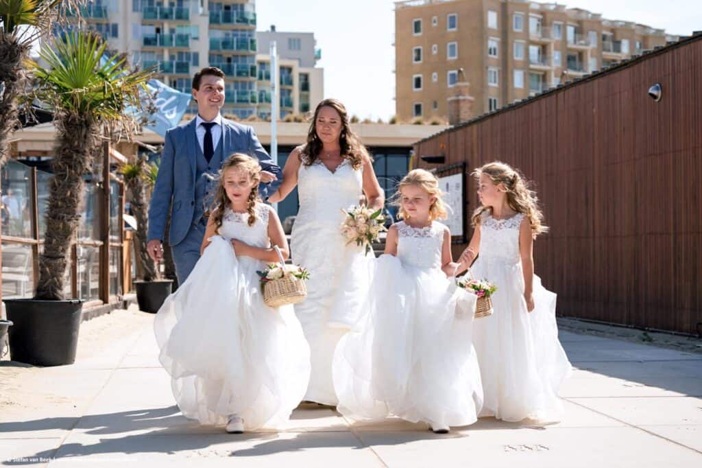 Bruid komt met zoon en drie bruidsmeisjes aangewandeld voor bruiloft op het strand van Scheveningen © Stefan van Beek Fotografie