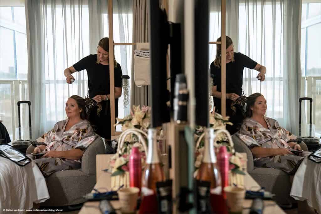 Bruid zit in de make-up tijdens voorbereidingen voor bruiloft bij trouwlocatie Strandrestaurant Werelds in hotelkamer Carlton Beach Hotel in Scheveningen © Stefan van Beek Fotografie