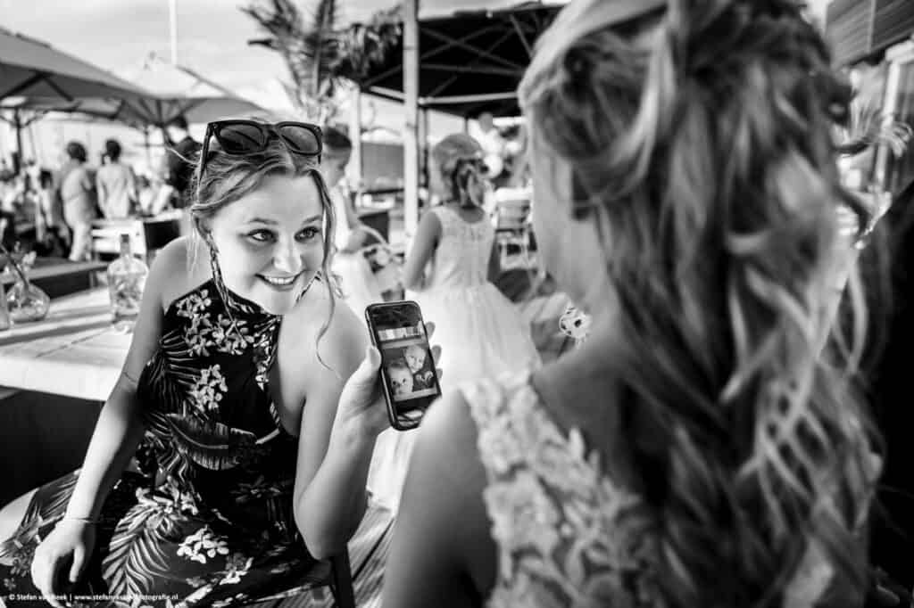 Bruidsgast laat met glimlach een foto op een mobieltje zien aan bruidsmeisje © Stefan van Beek Fotografie