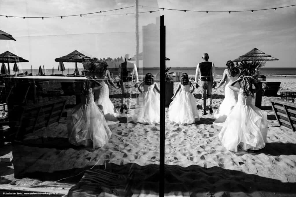 Bruidspaar en bruidsmeisjes wandelen richting het strand tijdens hun bruiloft in Scheveningen © Stefan van Beek Fotografie