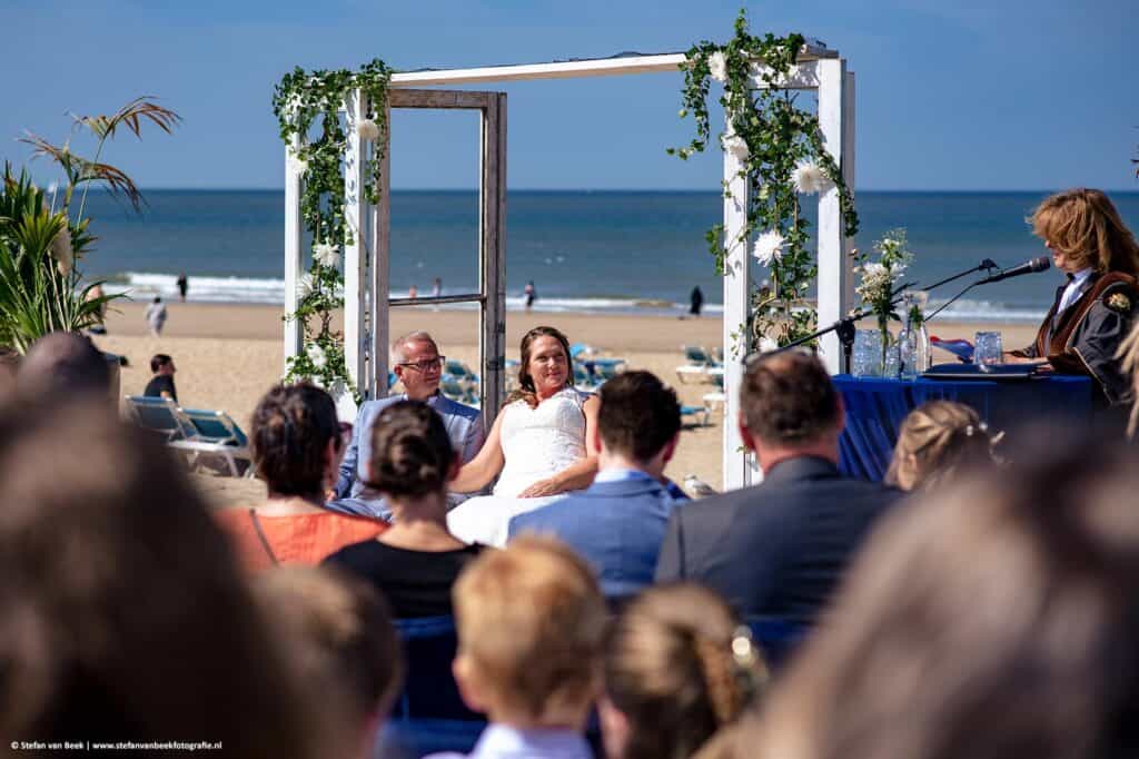 Bruidspaar tijdens ceremonie op strand van Scheveningen met zee op de achtergrond © Stefan van Beek Fotografie