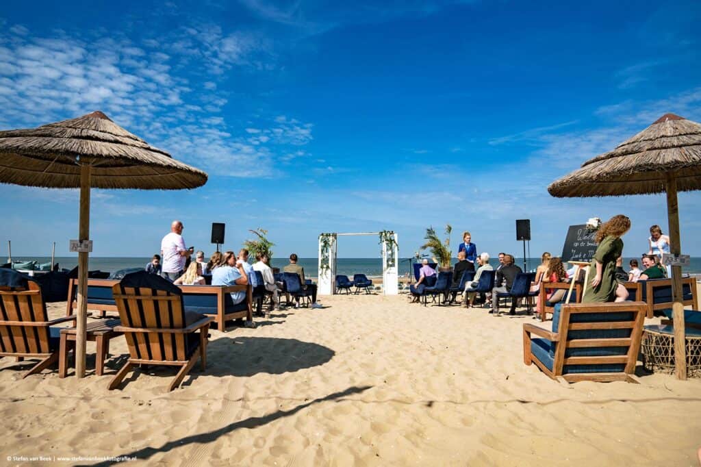 Ceremonie opstelling met gasten op zonnige dag met strakblauwe lucht bij trouwlocatie Strandrestaurant Werelds in Scheveningen © Stefan van Beek Fotografie