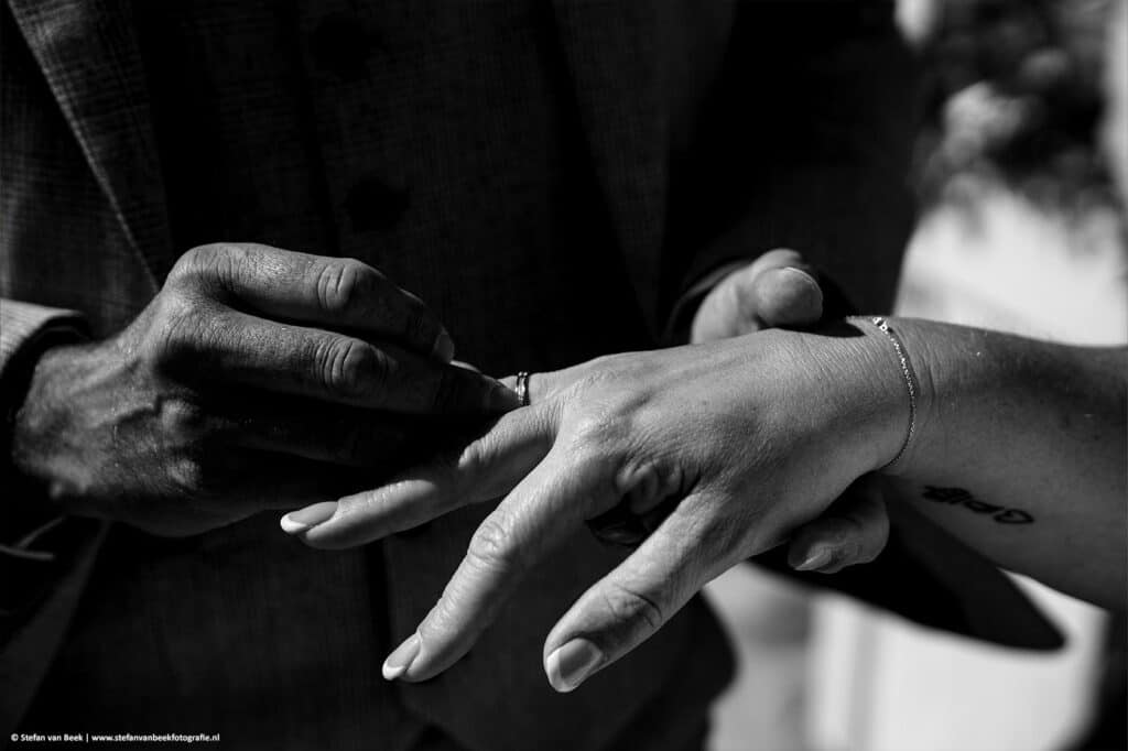 Close-up van bruidegom die ring om doet bij de bruid tijdens bruiloft op het strand © Stefan van Beek Fotografie