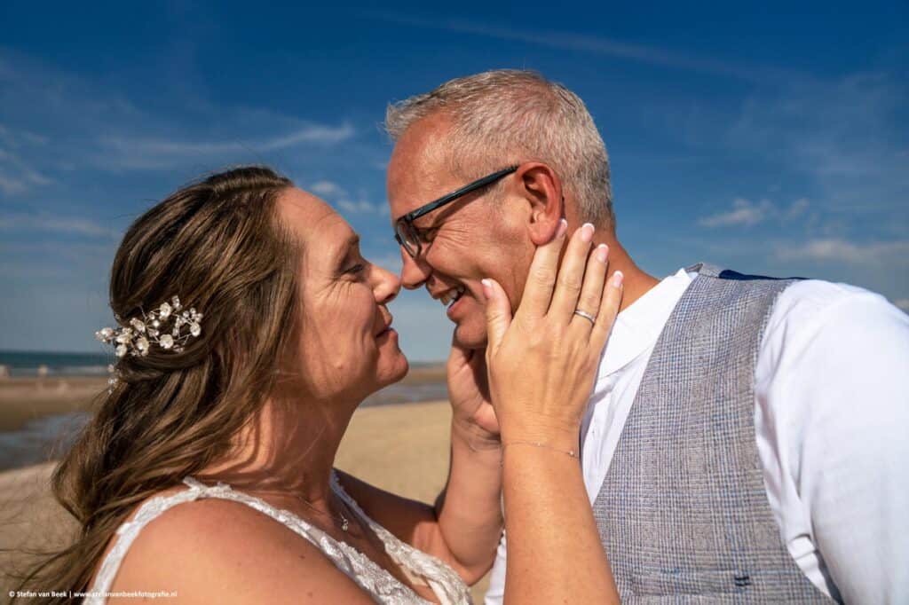 Close-up van bruidspaar met intieme blik net voordat ze elkaar een zoen geven tijdens bruiloft op het strand © Stefan van Beek Fotografie