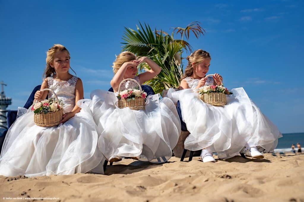 Drie bruidsmeisjes op een rij op het strand van Scheveningen tijdens een bruiloft © Stefan van Beek Fotografie