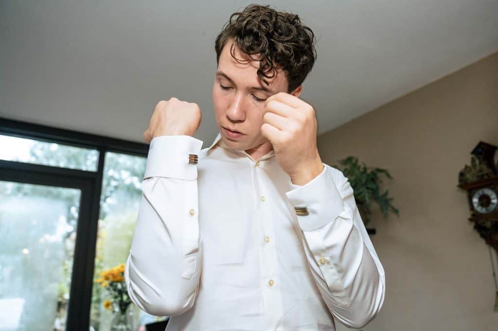 Bruidegom met zwart krullend haar heeft armen voor zich omhoog en kijkt naar manchetknopen op zijn shirt © bruidsfotograaf Stefan van Beek