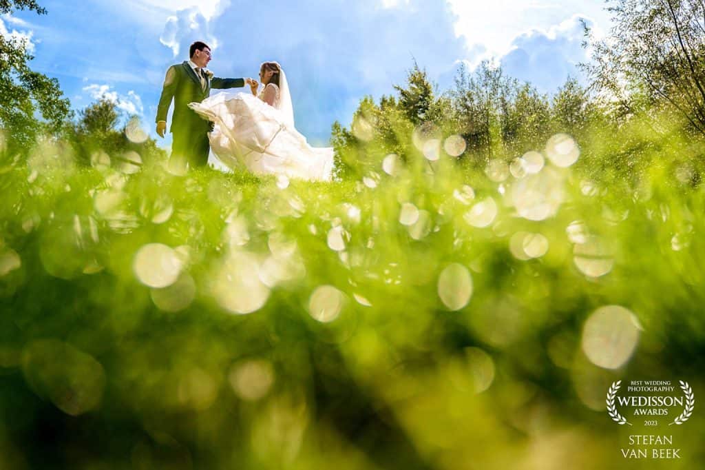 Wedisson Award Stefan van Beek wedding couple doing dance move on grass hill with bokeh balls and blue sky in background
