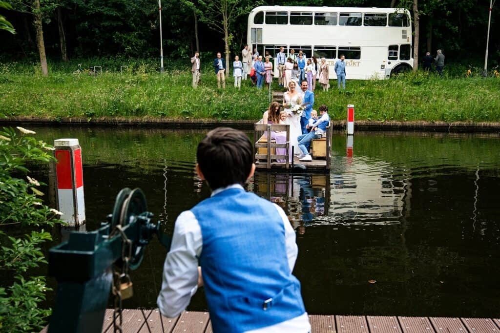 Bruidsjongen trekt vlot met bruidsgasten die uit de Witte Dubbeldekbus komen over het water naar de Waterkant in het Westbroekpark Den Haag © Stefan van Beek Fotografie